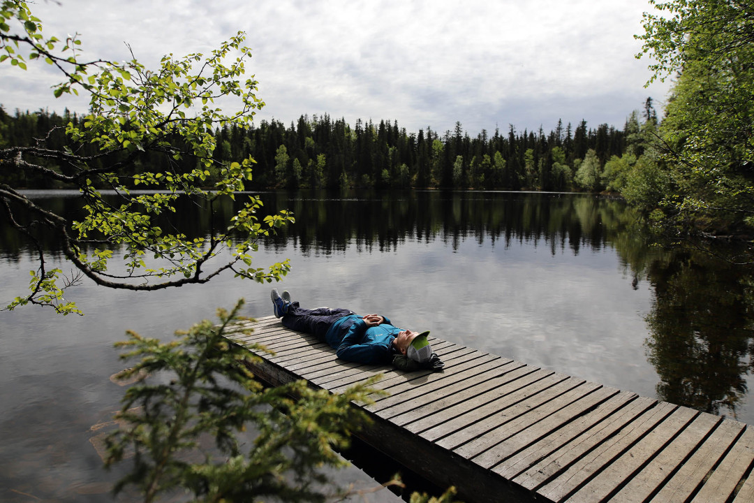 Retkeilijä rentoutuu lammen rannassa laiturilla
