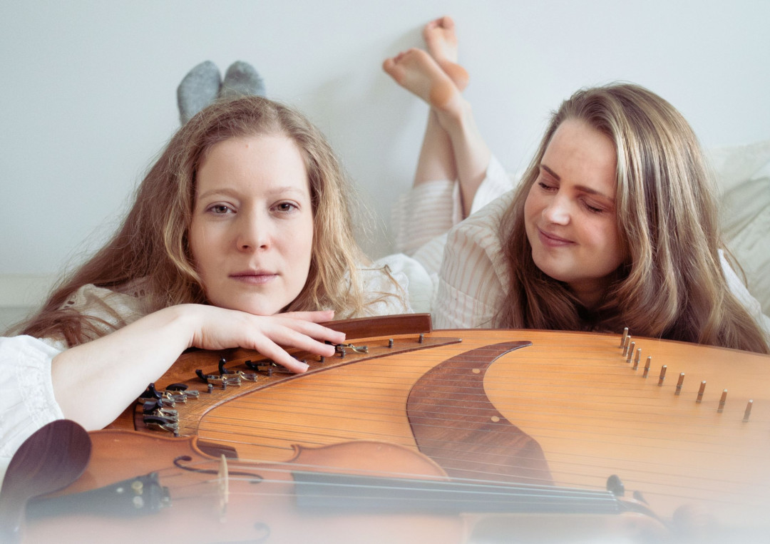 Kuvassa Lotta Aakko ja Aurora Visa makaavat kantele edessään valkoisissa vaatteissa.