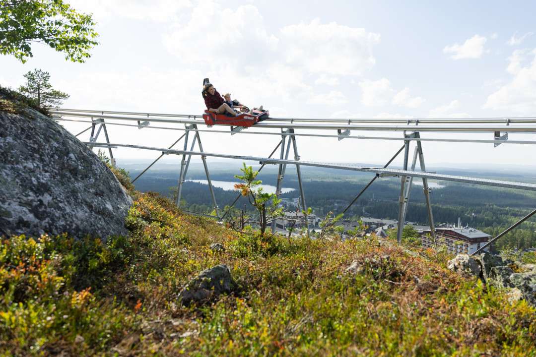 Aikuinen ja lapsi laskevat Rukan kesäkelkkaradalla maisemien ympäröimänä.