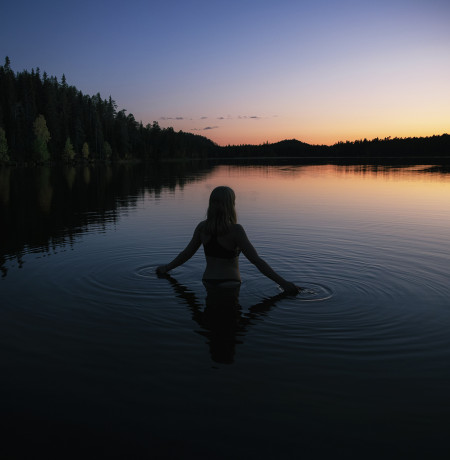 Nainen uimassa järvessä auringonlaskun aikaan