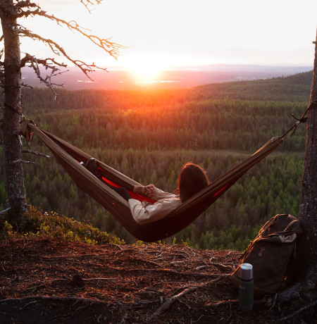 Nainen riippumatossa ihailee auringonlaskua.