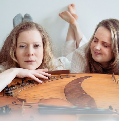 Kuvassa Lotta Aakko ja Aurora Visa makaavat kantele edessään valkoisissa vaatteissa.