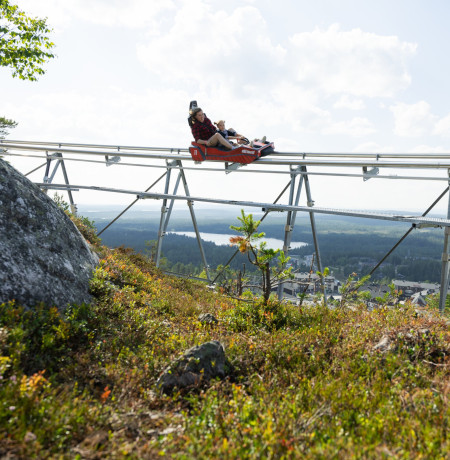 Aikuinen ja lapsi laskevat Rukan kesäkelkkaradalla maisemien ympäröimänä.