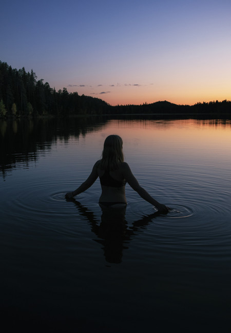 Nainen uimassa järvessä auringonlaskun aikaan