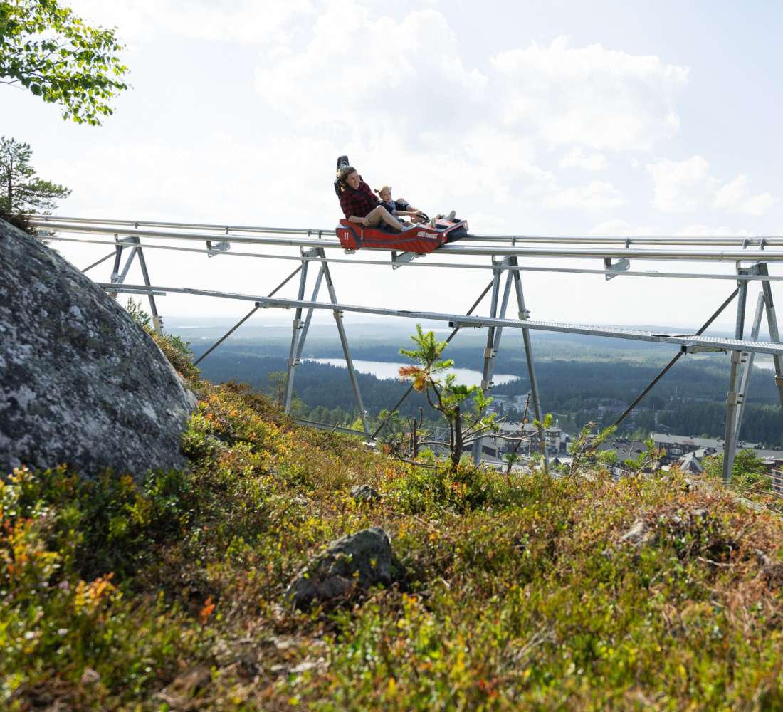 Aikuinen ja lapsi laskevat Rukan kesäkelkkaradalla maisemien ympäröimänä.