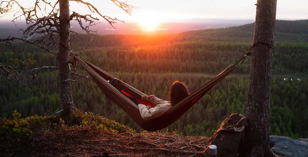 Nainen riippumatossa ihailee auringonlaskua.