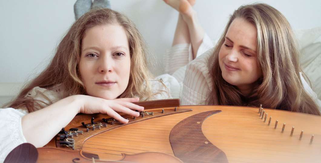 Kuvassa Lotta Aakko ja Aurora Visa makaavat kantele edessään valkoisissa vaatteissa.