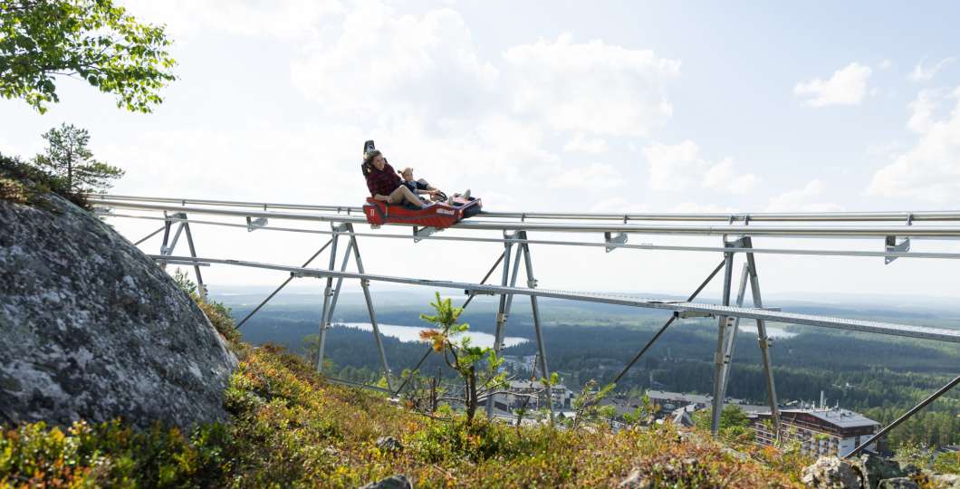 Aikuinen ja lapsi laskevat Rukan kesäkelkkaradalla maisemien ympäröimänä.