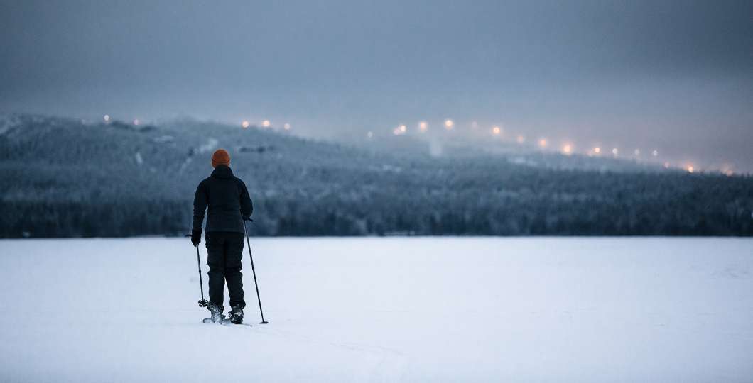 Nainen hiihtää järven jäällä, Rukan valot taustalla